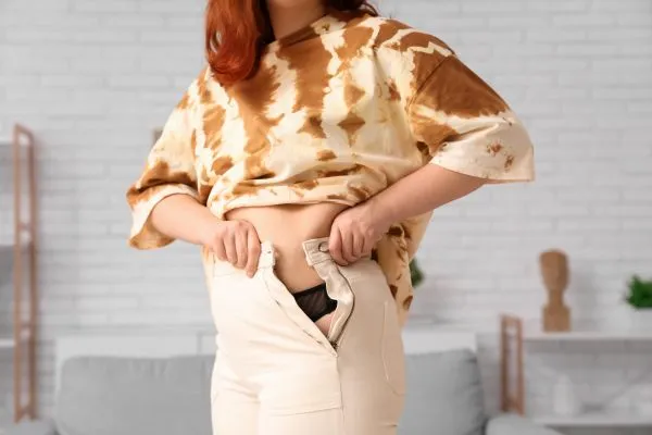 Image of woman trying to do her trousers up after pregnancy weight gain Ross-on-Wye